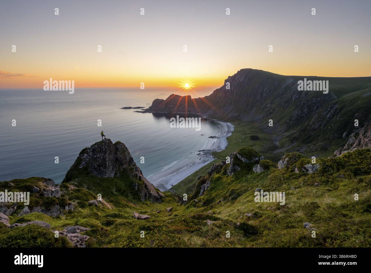 Arrampicati sulle rocce di fronte al pittoresco paesaggio, ammira il paesaggio costiero al tramonto, le scogliere e la cima di Matind o Matinden, la spiaggia di Hoyvika e. Foto Stock