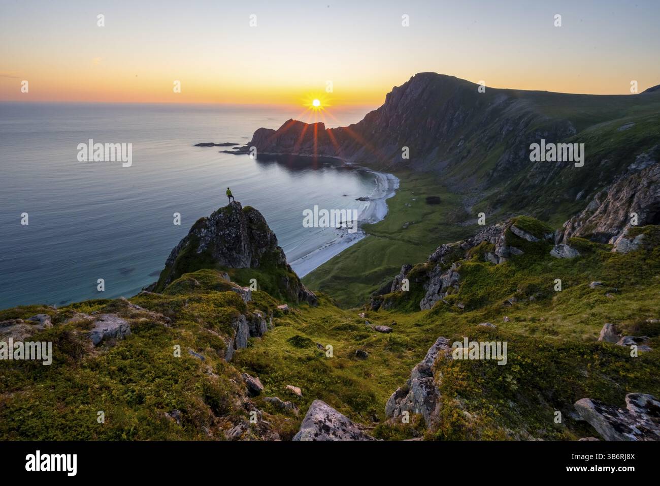 Arrampicati sulle rocce di fronte al pittoresco paesaggio, ammira il paesaggio costiero al tramonto, le scogliere e la cima di Matind o Matinden, la spiaggia di Hoyvika e. Foto Stock