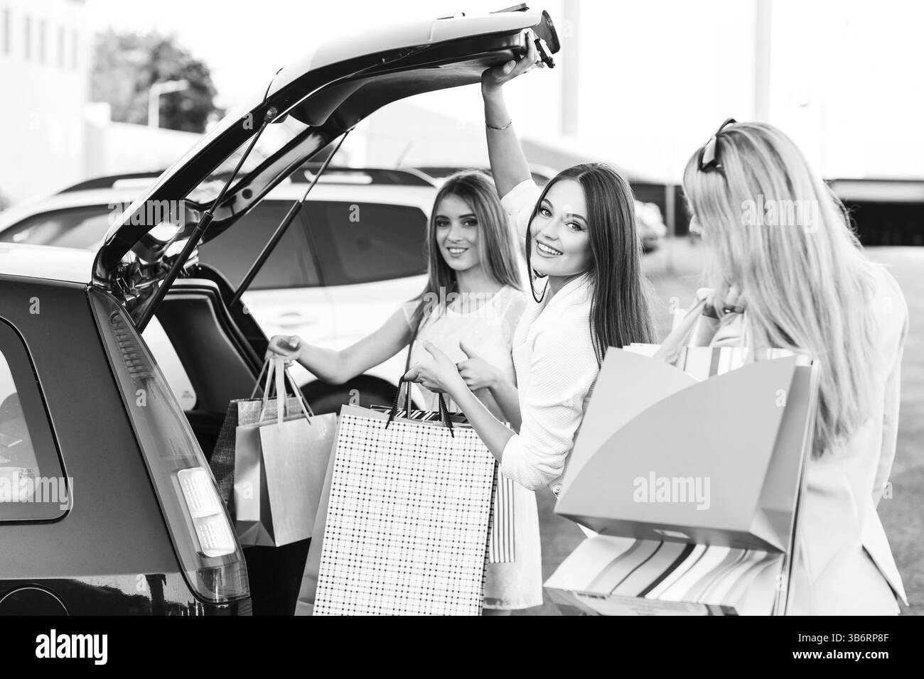 Gruppo di ragazze dopo aver fatto shopping caricando una borsa della spesa nel bagagliaio di un'auto Foto Stock