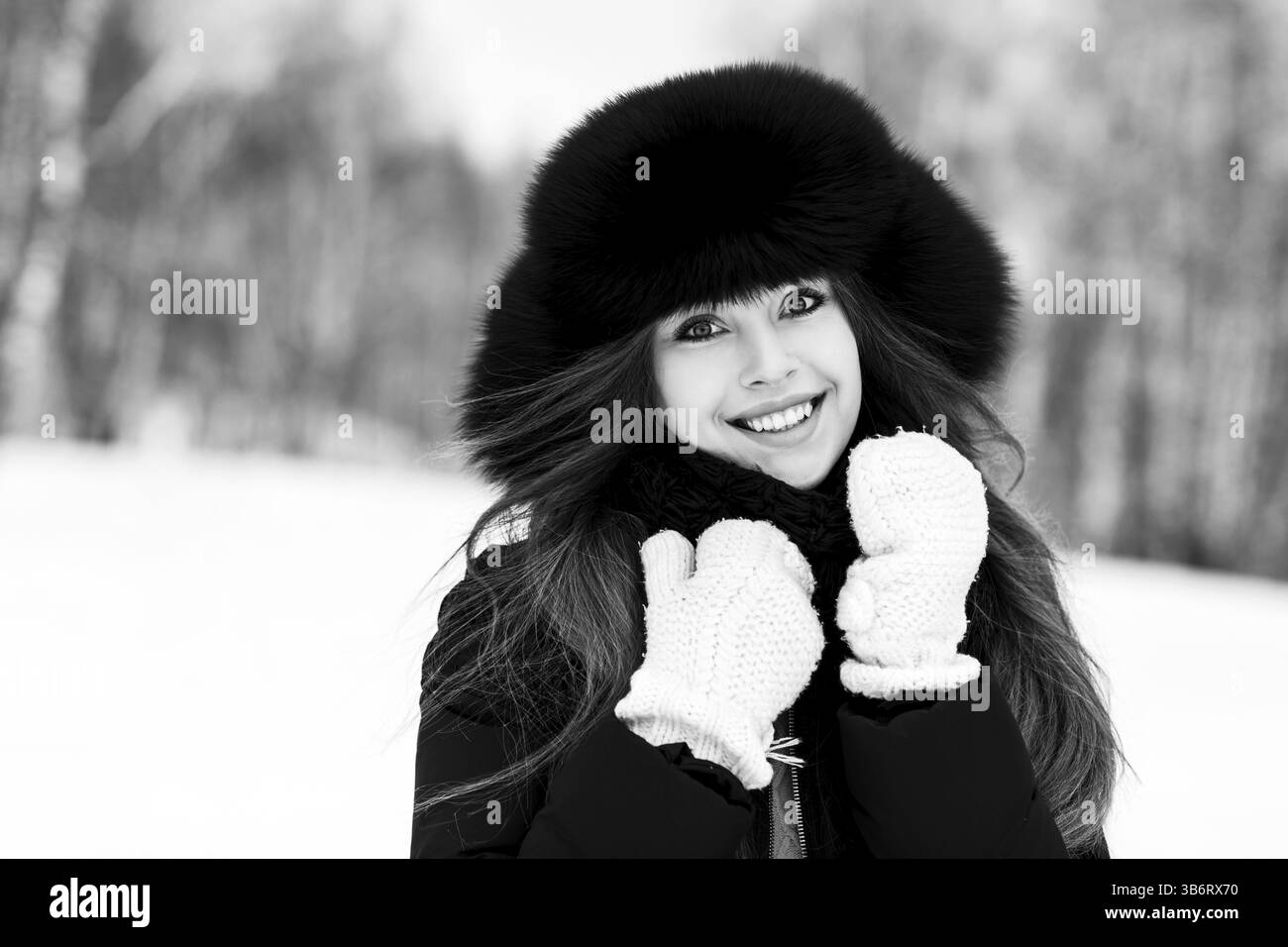 Ritratto di una giovane donna sorridente in un lussuoso panno in pelliccia all'aperto in inverno in bianco e nero Foto Stock