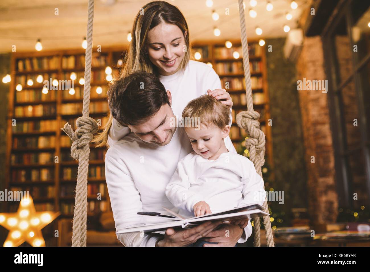 Insieme di famiglia. Mamma, papà e figlio leggono insieme un libro di storie seduti a casa la sera dello swing. Concetto di famiglia e genitorialità. La famiglia felice legge Foto Stock