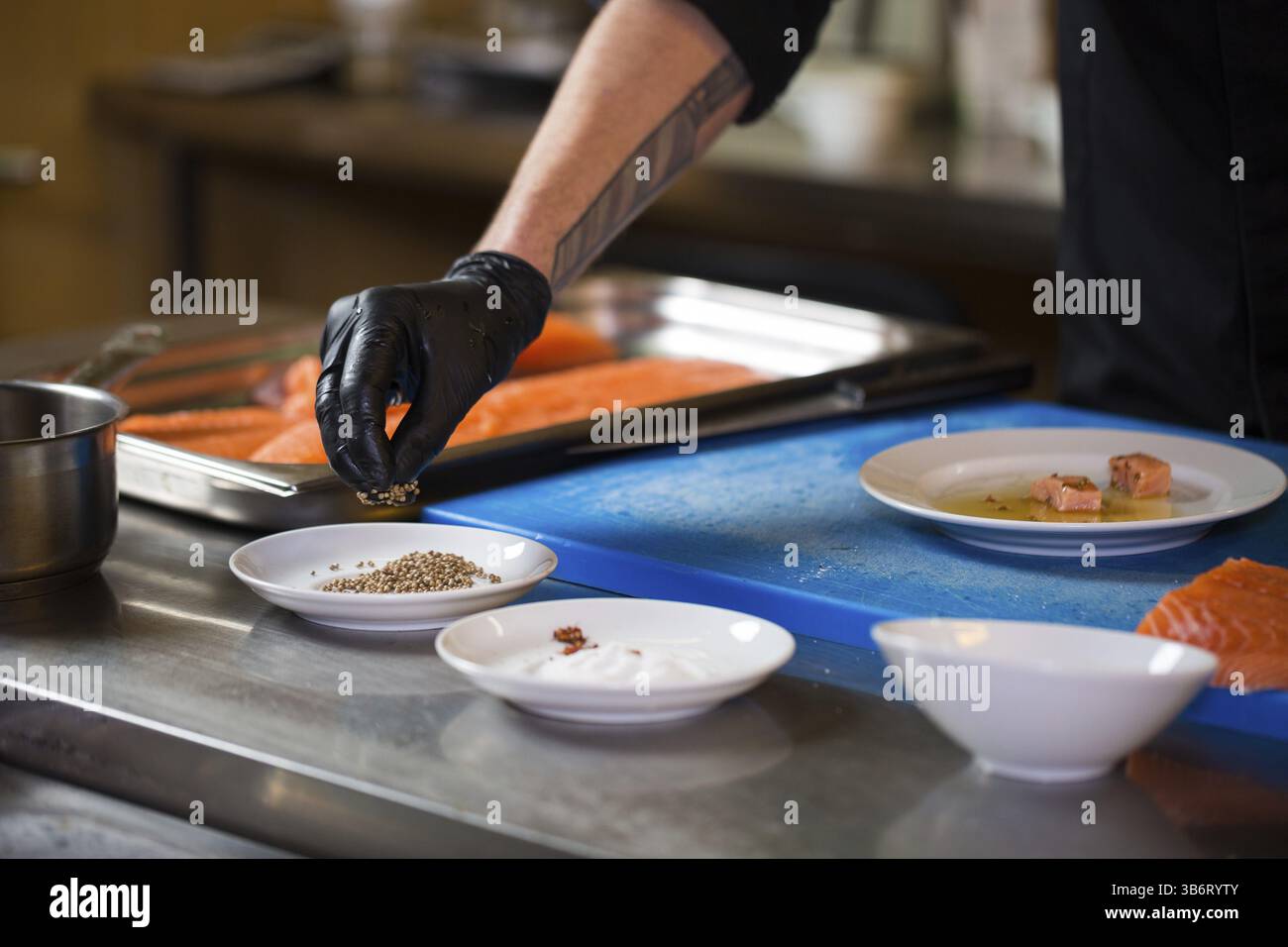 Cucina a tema è una professione di cottura. Close-up di un uomo caucasico la mano in un ristorante di cucina Preparazione di filetti di pesce rosso salmone carne in black l Foto Stock