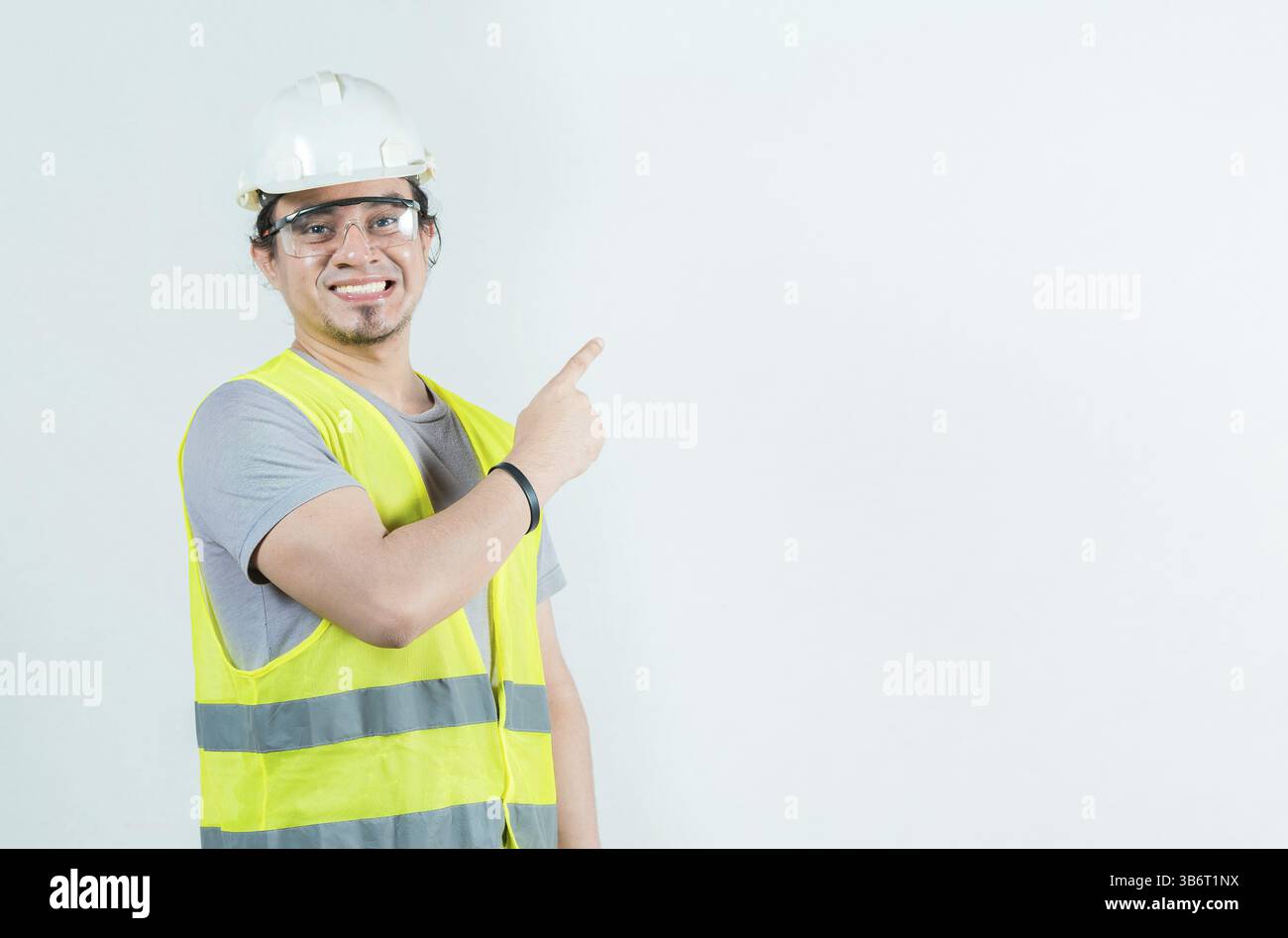 Felice costruttore maschio che punta al lato isolato. Lavoratore edile sorridente che indica lo spazio vuoto Foto Stock