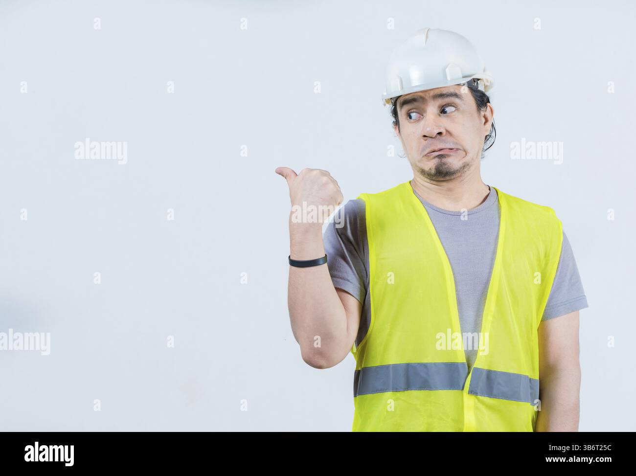 Divertente operaio edile che indica uno spazio vuoto isolato. Il costruttore ha sorpreso a indicare uno spazio pubblicitario isolato Foto Stock