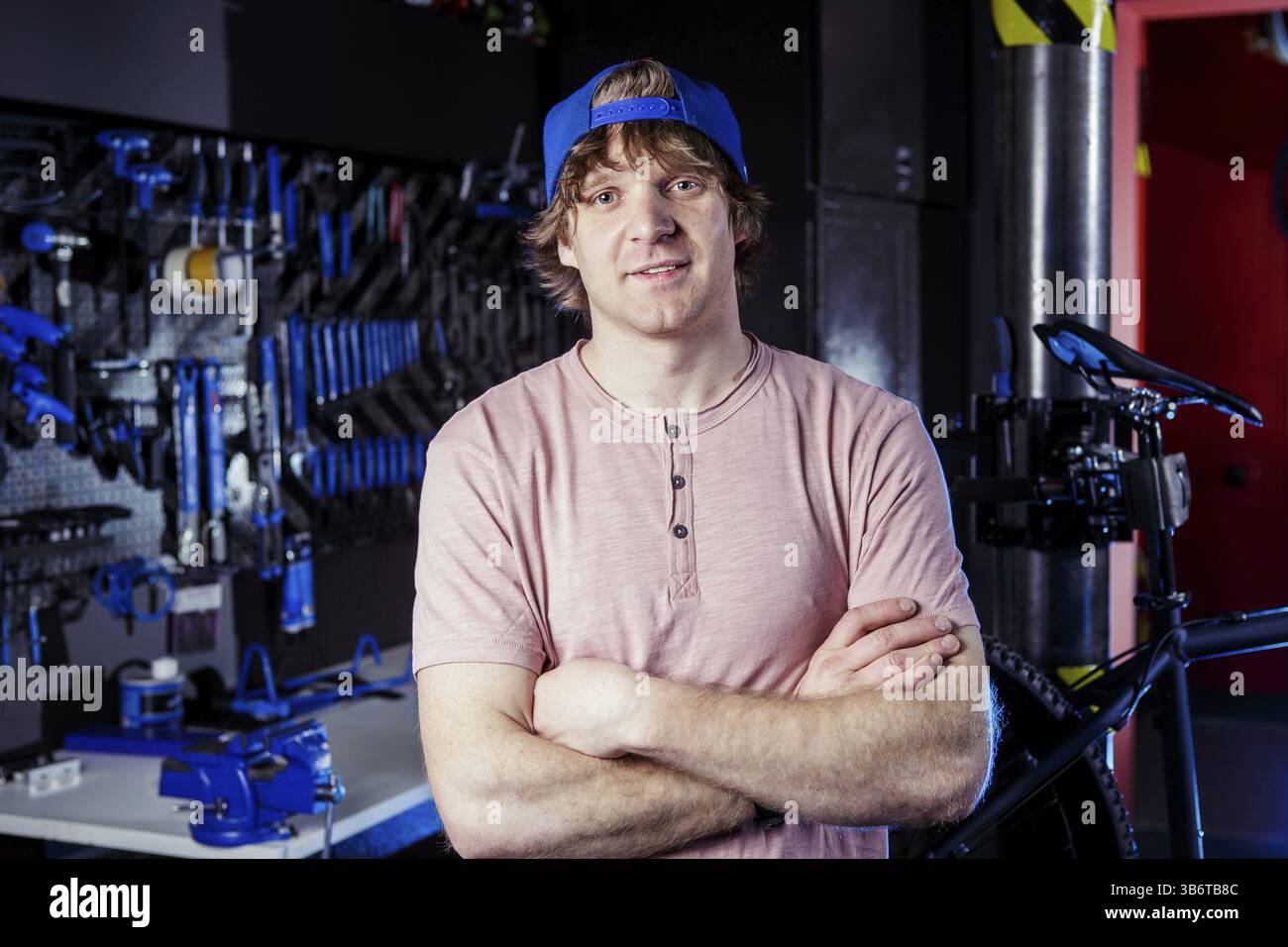 Servizio di trasporto per piccole imprese e biciclette. ritratto di un giovane uomo in un berretto che posa sullo sfondo di un laboratorio di biciclette e di uno strumento per sistemarsi Foto Stock