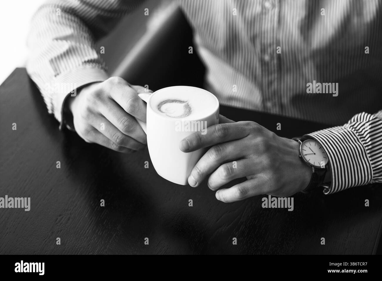 Imprenditore prendendo una pausa in ufficio come egli gode di una tazza calda di caffè aromatico, vista ravvicinata delle sue mani Foto Stock