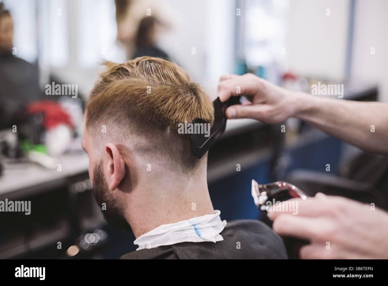 Immagine ravvicinata di un uomo di ottenere un taglio di capelli alla moda in un salone di parrucchiere. Maschio parrucchiere caucasici che serve un client. Con barba rendendo taglio di capelli con un t Foto Stock
