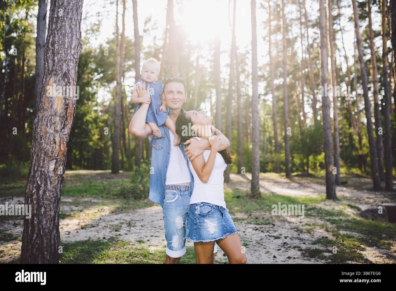 Famiglia mamma, papà e la figlia si siede al papà sulle spalle e genitori bacio sulla natura della foresta in estate al tramonto Foto Stock