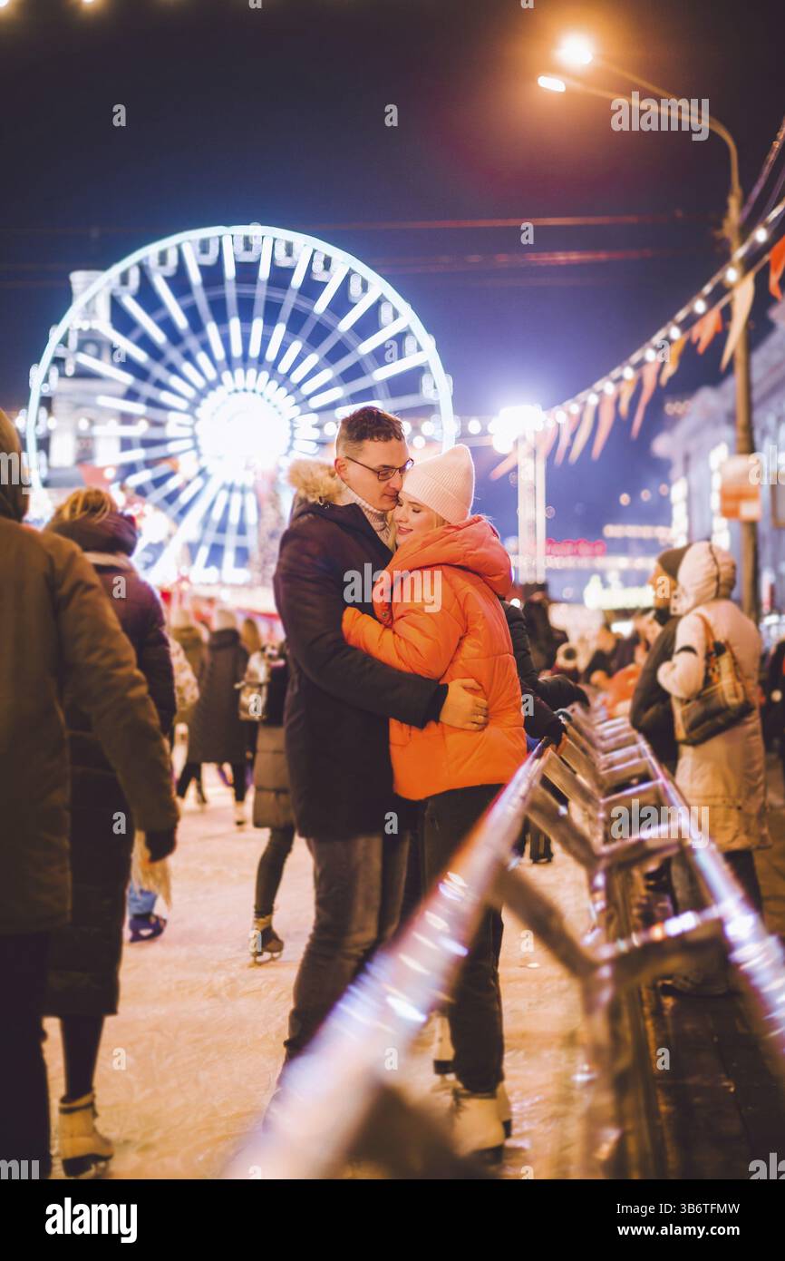 Una bella coppia si diverte nell'arena del ghiaccio. Pattinaggio su ghiaccio attivo sulla pista di pattinaggio serale nella piazza della città in inverno la vigilia di Natale. San Valentino al Foto Stock