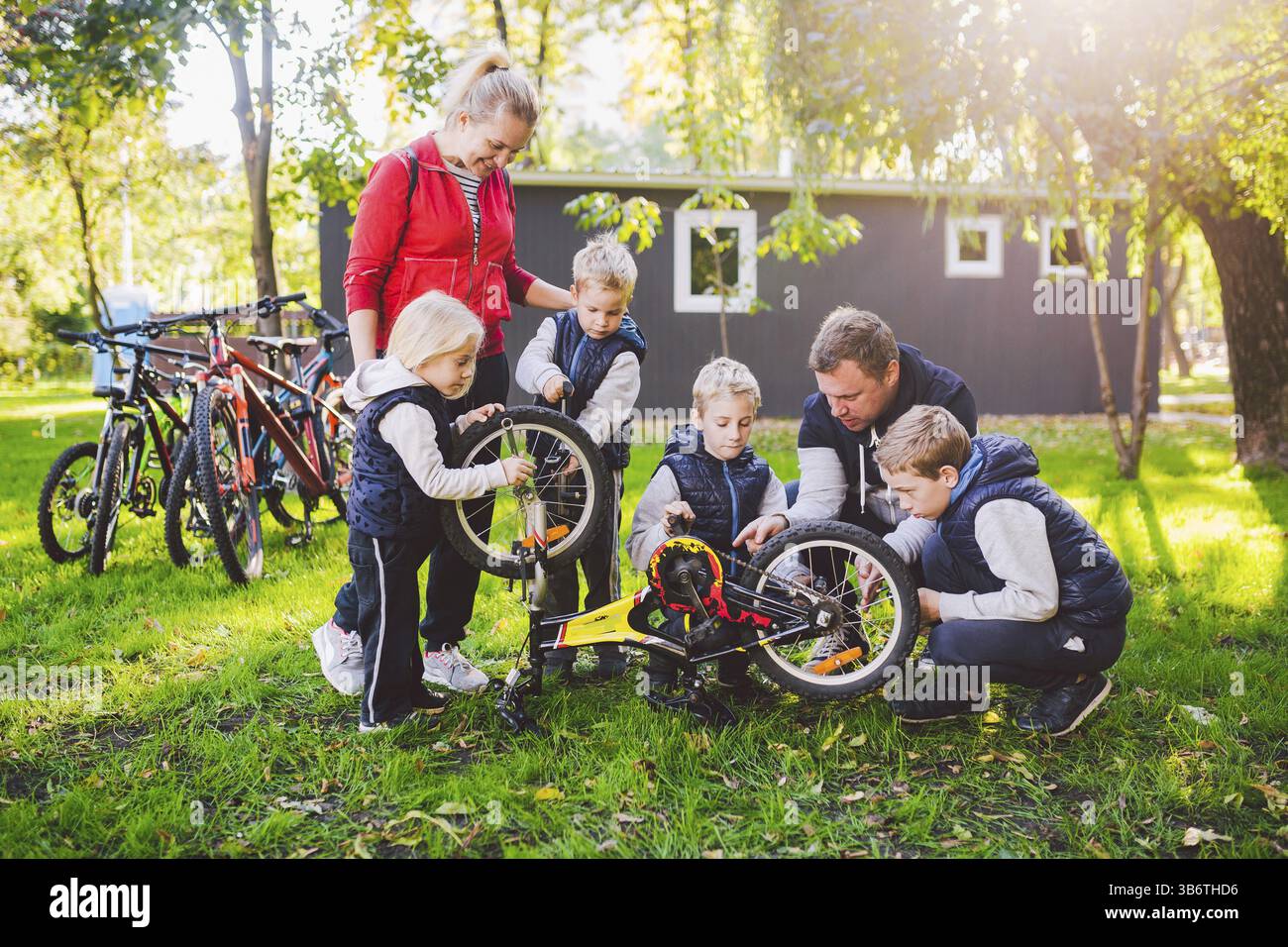 Il tema è il lavoro di squadra e uno spirito familiare. Risolvere i problemi insieme. Famiglia numerosa e cordiale che ripara una bicicletta nel parco. Papà e mamma insegnano c Foto Stock