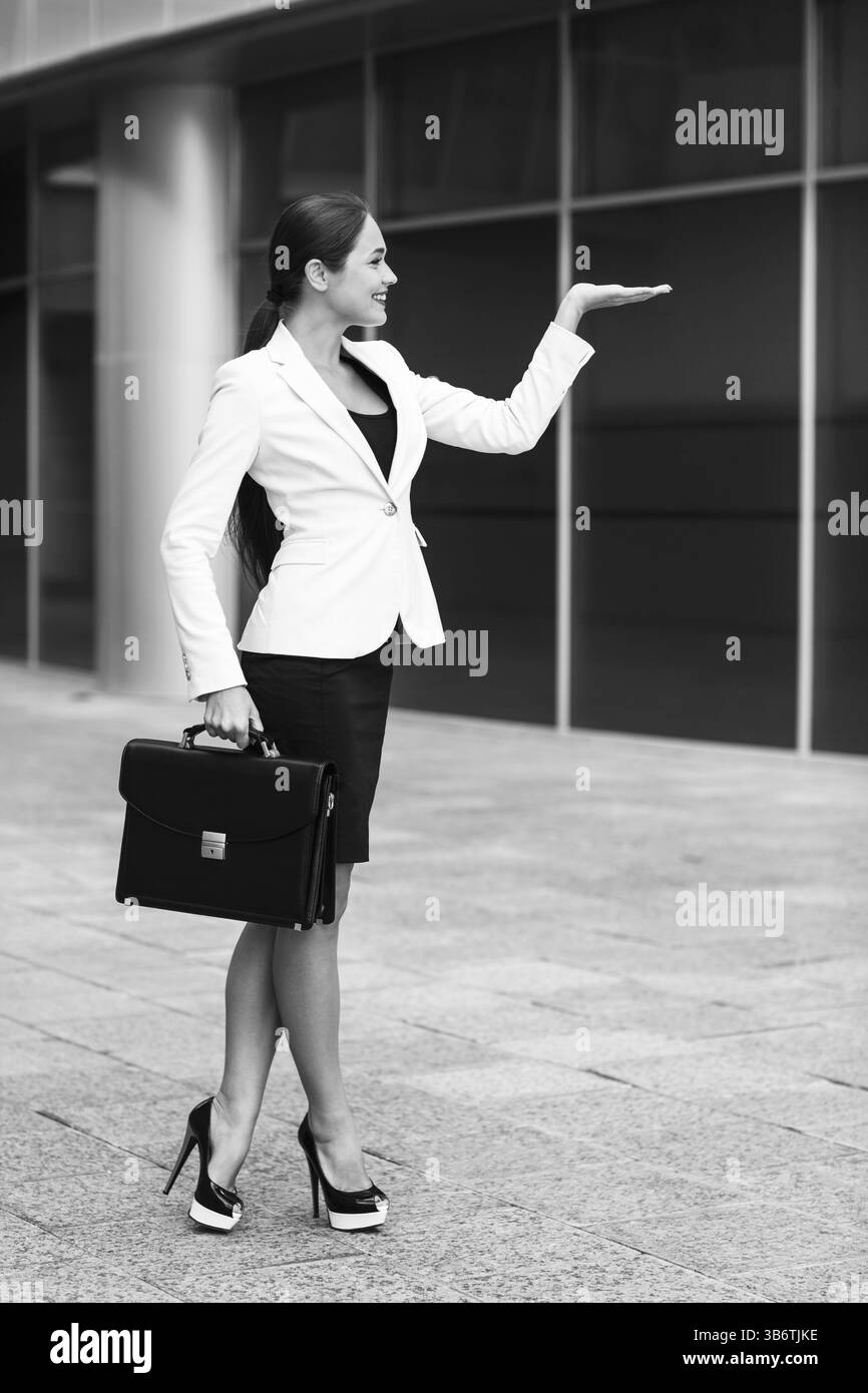 A piena lunghezza Ritratto di sorridere business donna con valigetta presentare qualcosa su vuoto palm Foto Stock