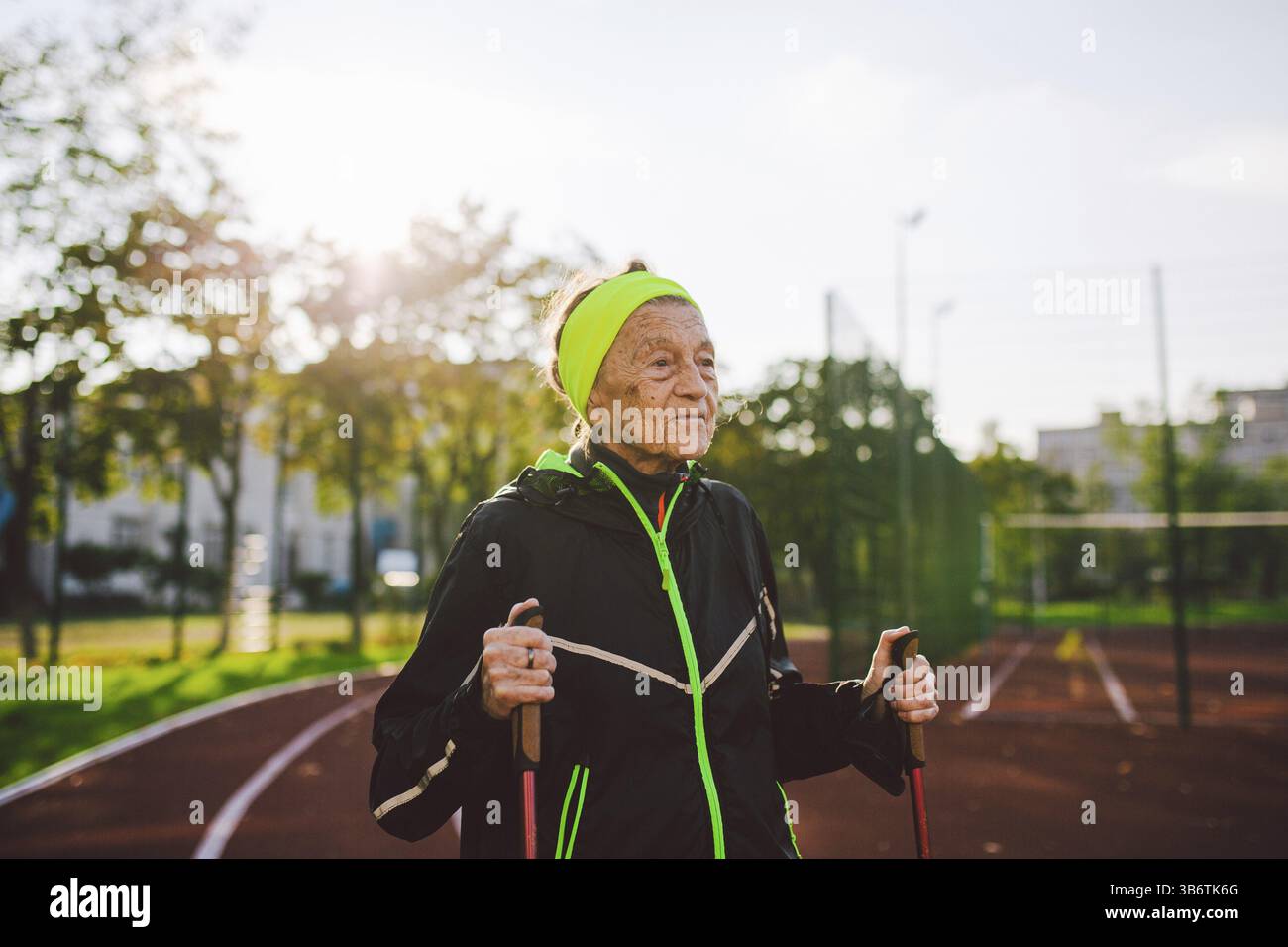 Anziani attivi le donne anziane caucasiche di 90 anni praticano il nordic walking con i pali di sci su una pista con un rivestimento di gomma rossa. Vacanze attive. Un adattamento Foto Stock