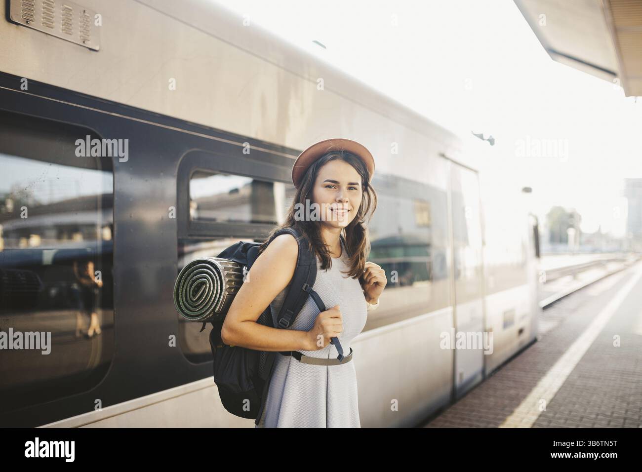 Ferrovia a tema e viaggi. ritratti la giovane donna caucasica con un sorriso sorridente in piedi alla stazione ferroviaria sullo sfondo con zaino e attrezzature per Foto Stock