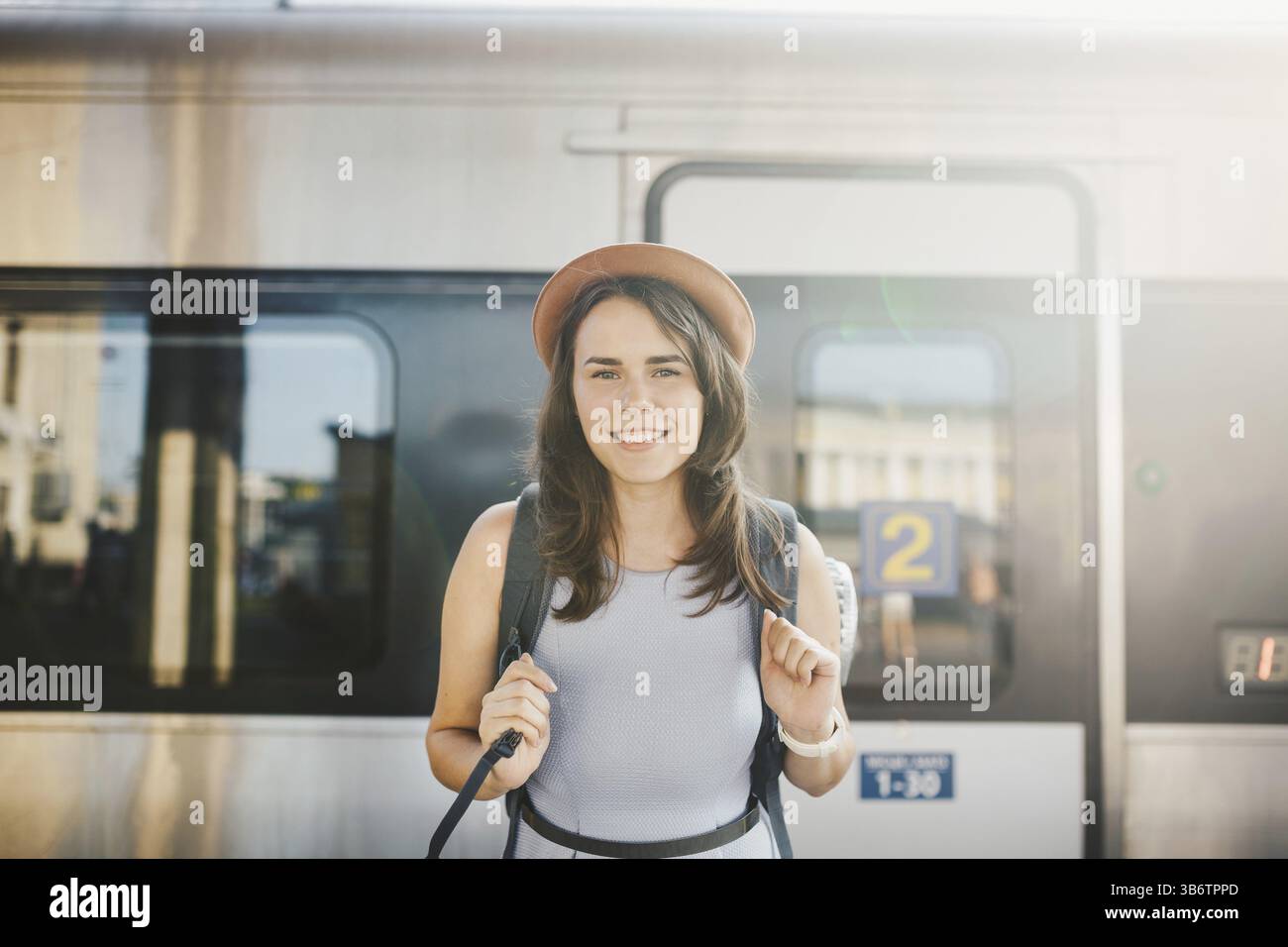 Ferrovia a tema e viaggi. ritratti la giovane donna caucasica con un sorriso sorridente in piedi alla stazione ferroviaria sullo sfondo con zaino e attrezzature per Foto Stock