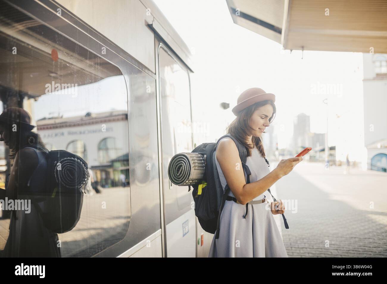 Trasporto e viaggio a tema. ritratti la giovane donna caucasica con sorriso in piedi in piedi sulla stazione ferroviaria sullo sfondo con zaino utilizzando il technolo Foto Stock