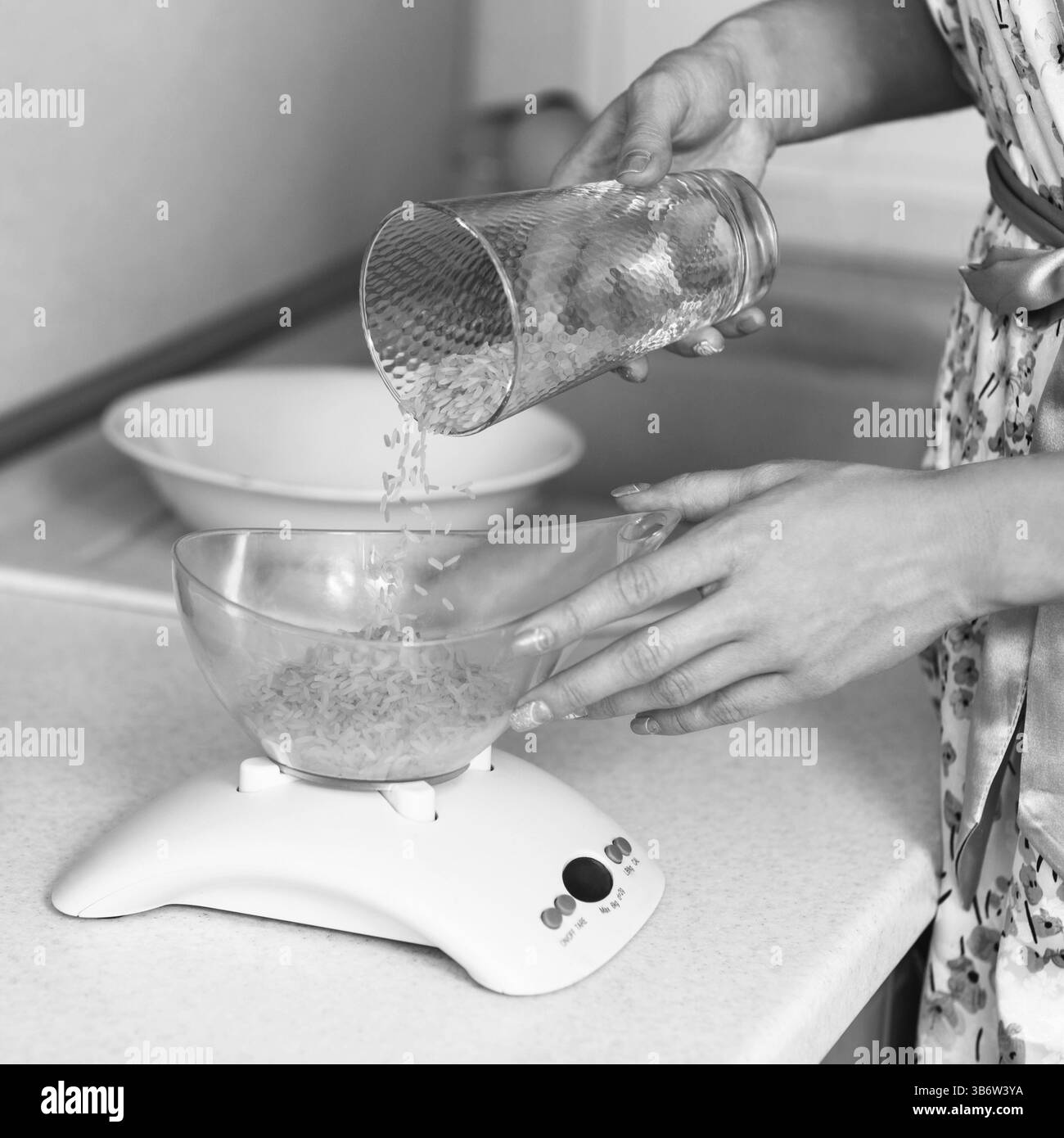 La donna setaccia il riso in una ciotola sulla bilancia da cucina Foto Stock