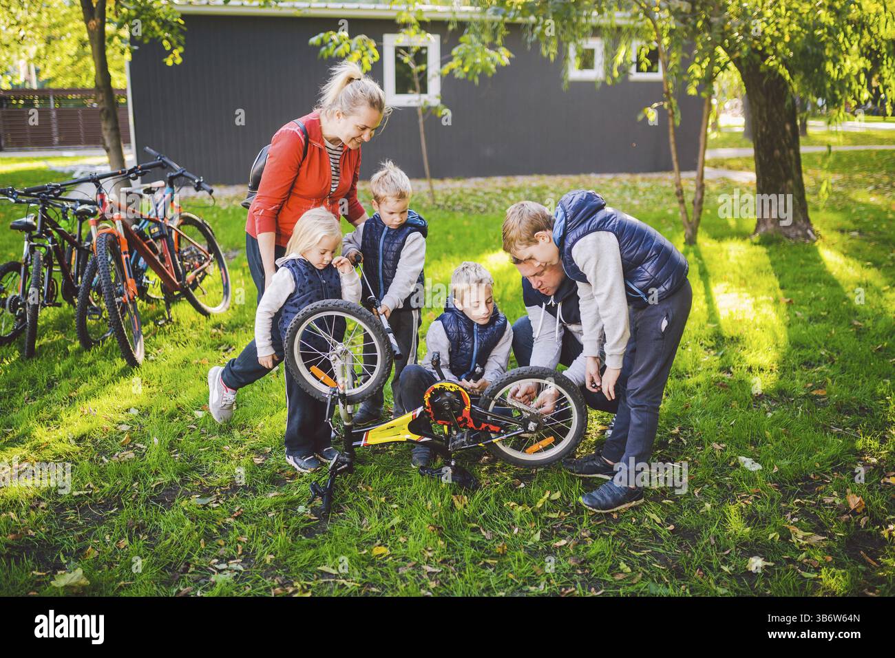 Il tema è il lavoro di squadra e uno spirito familiare. Risolvere i problemi insieme. Famiglia numerosa e cordiale che ripara una bicicletta nel parco. Papà e mamma insegnano c Foto Stock