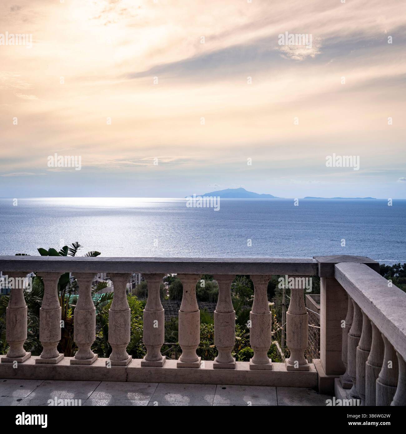 Una tranquilla vista costiera da un balcone in pietra che si affaccia su un mare calmo e isole lontane sotto un cielo nuvoloso. Foto Stock