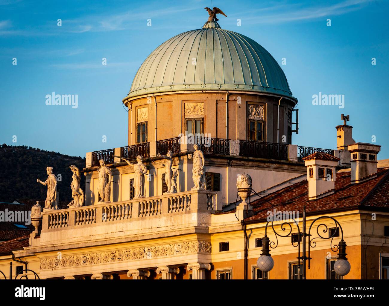 Una vista ravvicinata di un edificio storico caratterizzato da una cupola con un tetto di rame verde e statue lungo il tetto. L'edificio è illuminato da un caldo su Foto Stock