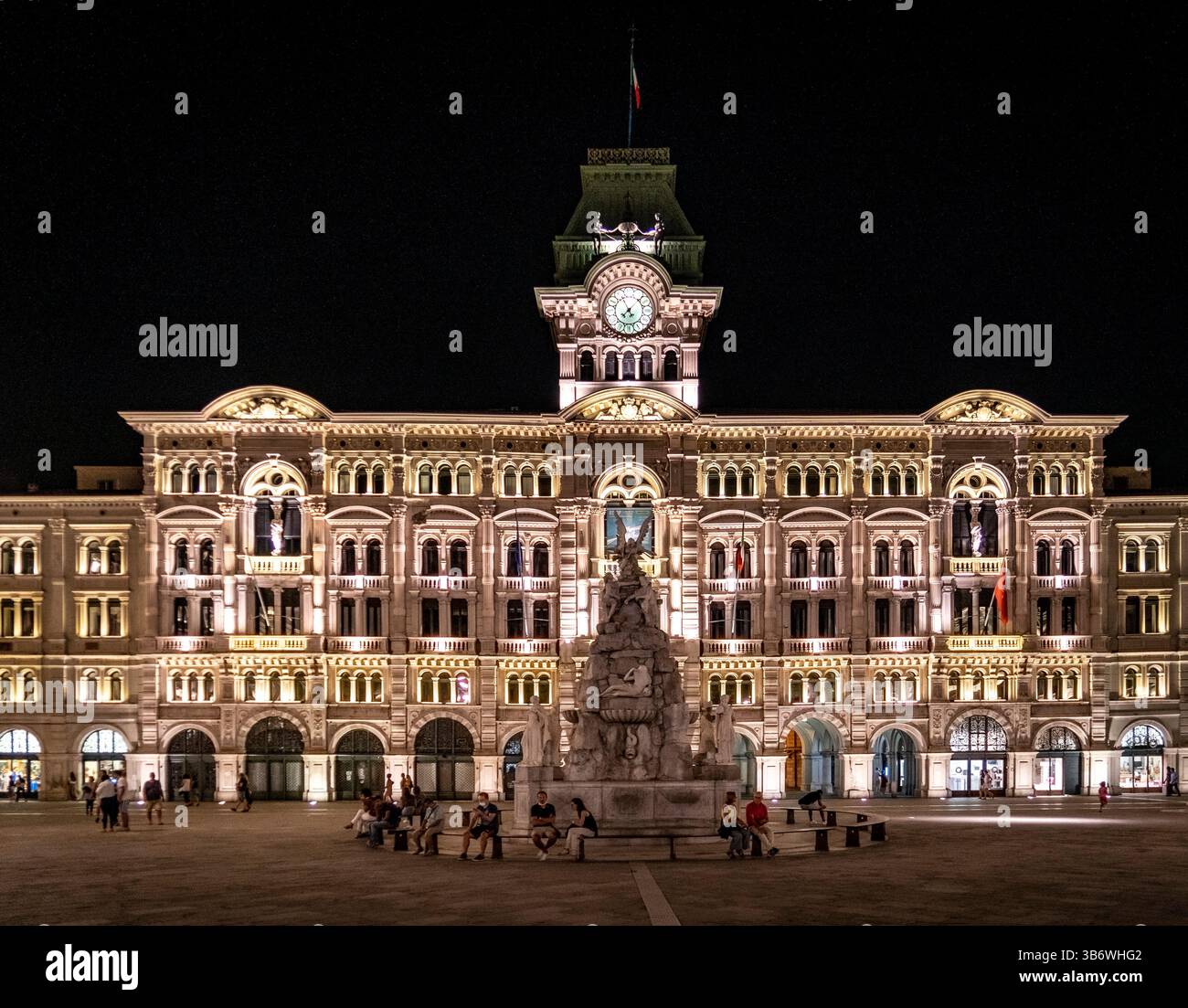 Un edificio storico splendidamente illuminato di notte, caratterizzato da intricati dettagli architettonici e un'importante torre dell'orologio. La gente si riunisce nella acqua Foto Stock