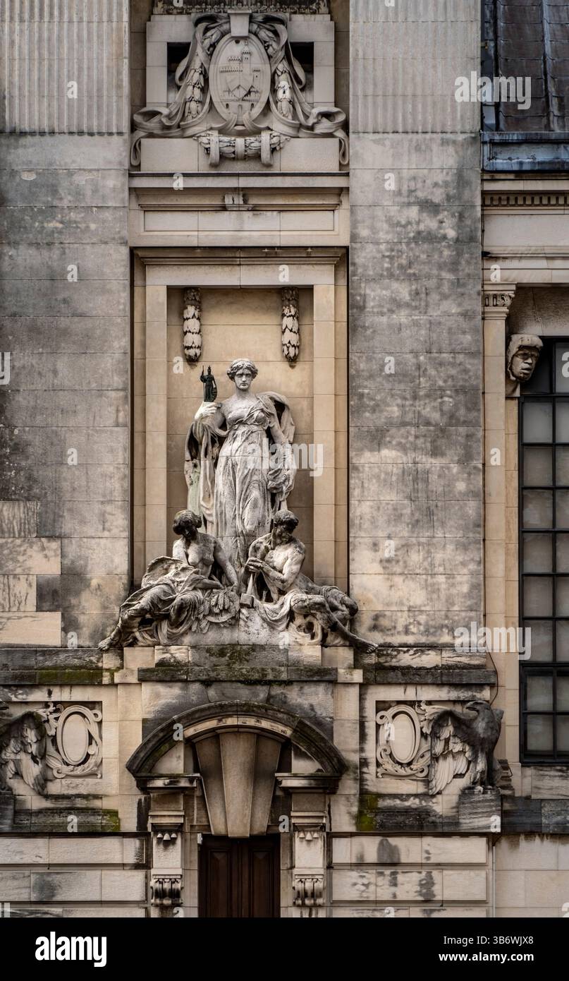 Una dettagliata scultura in pietra su una facciata dell'edificio, raffigurante una figura centrale circondata da figure più piccole. L'architettura presenta elementi classici Foto Stock
