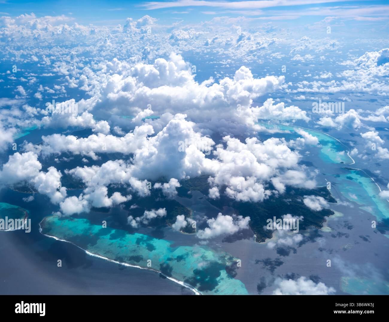 La splendida isola di Tahaa, circondata da una laguna turchese e da una barriera corallina, emerge attraverso nuvole sparse nel vasto Oceano Pacifico. Un respiro Foto Stock