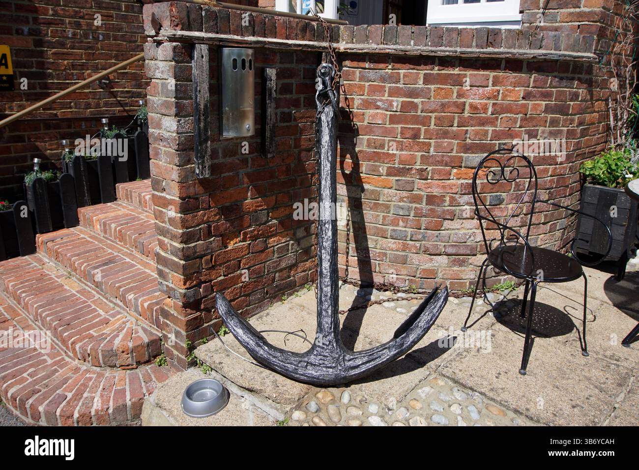 Vecchia ancora della nave usata come elemento decorativo all'esterno di un edificio in mattoni in una città costiera inglese. Rye, Sussex, Inghilterra Foto Stock