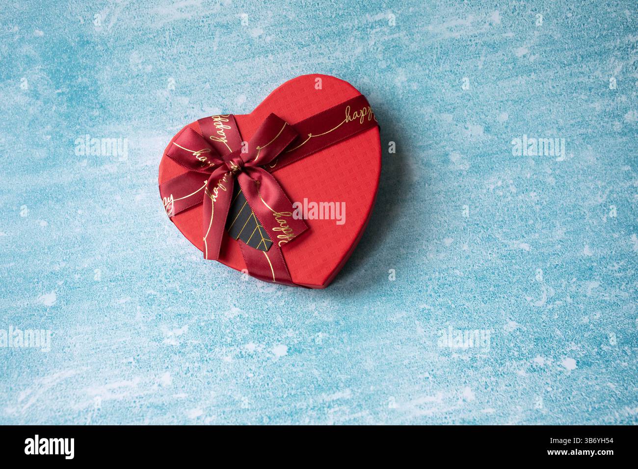 confezione regalo a forma di cuore con nastro su sfondo blu. Il concetto è adatto a storie d'amore, compleanni e San Valentino Foto Stock