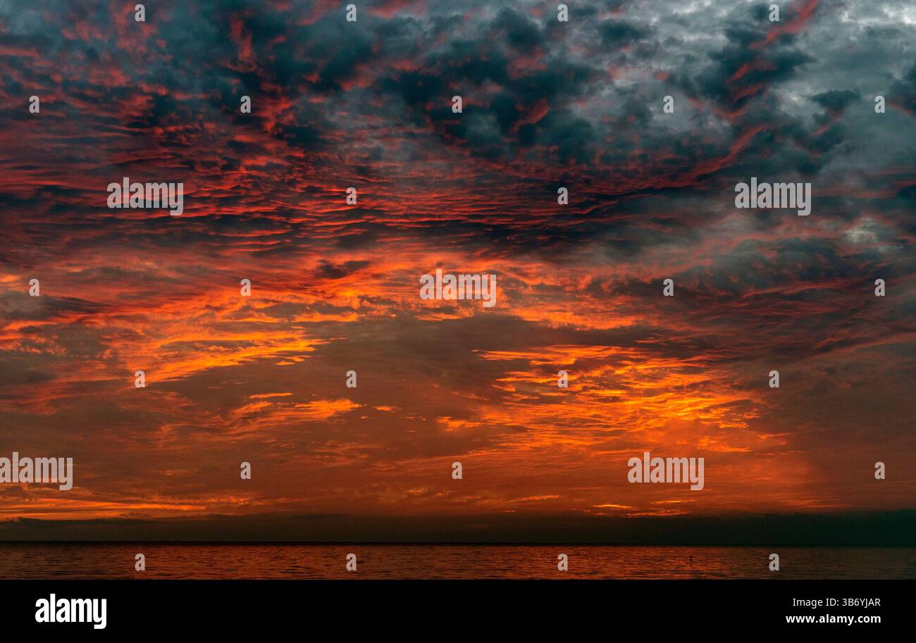 Un tramonto spettacolare sull'oceano, caratterizzato da vivaci sfumature arancione e rosso che si fondono con nuvole scure. Il cielo è pieno di nuvole testurizzate, creando un Foto Stock