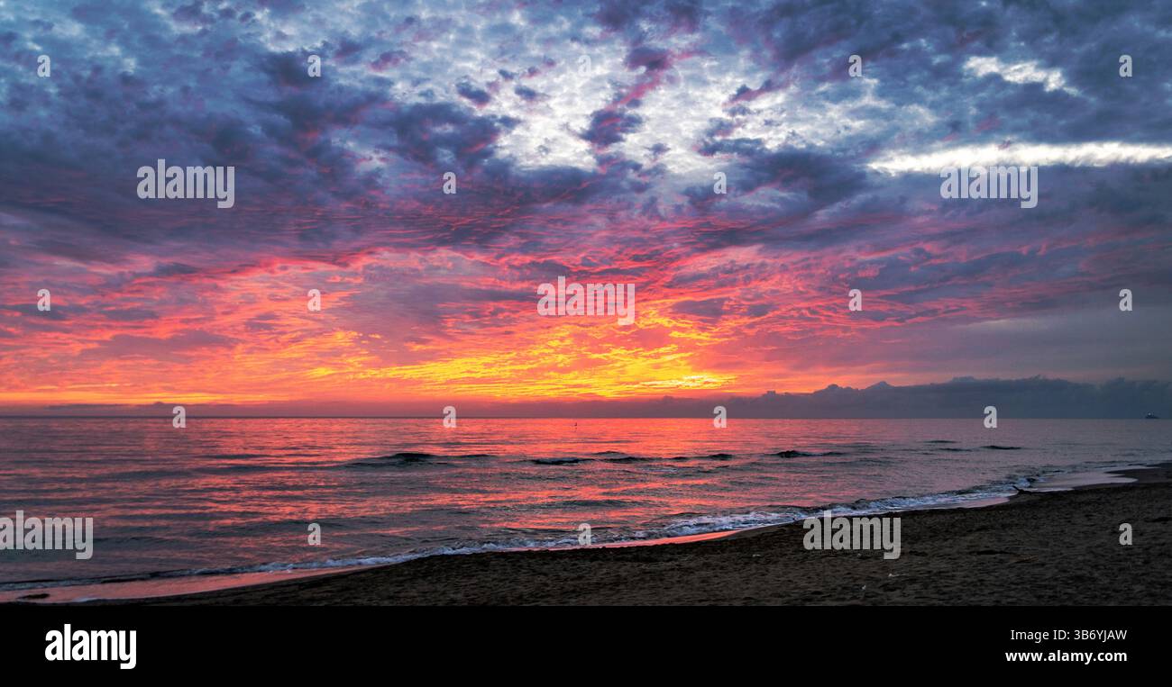 Un tramonto mozzafiato sull'oceano, con colori vivaci di arancio, rosa e viola che si riflettono sull'acqua. Il cielo è pieno di nuvole drammatiche, Foto Stock