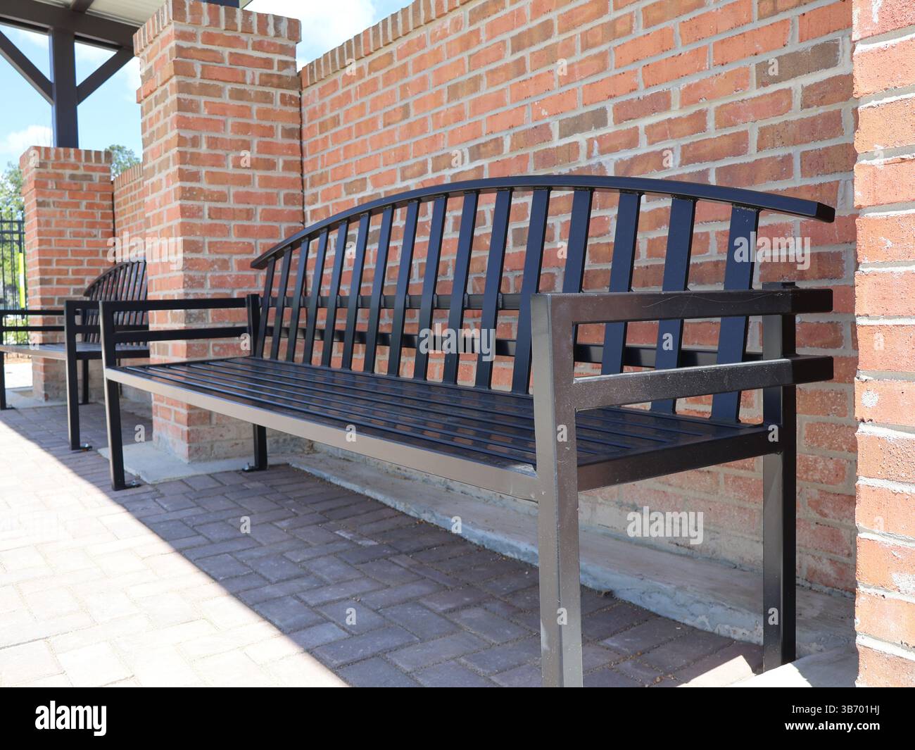 panchine in metallo nero con sedili e schienali a doghe ancorati a lastricatrici in mattoni vicino a mattoni rossi in un tradizionale motivo in muratura con una vista ravvicinata di l Foto Stock