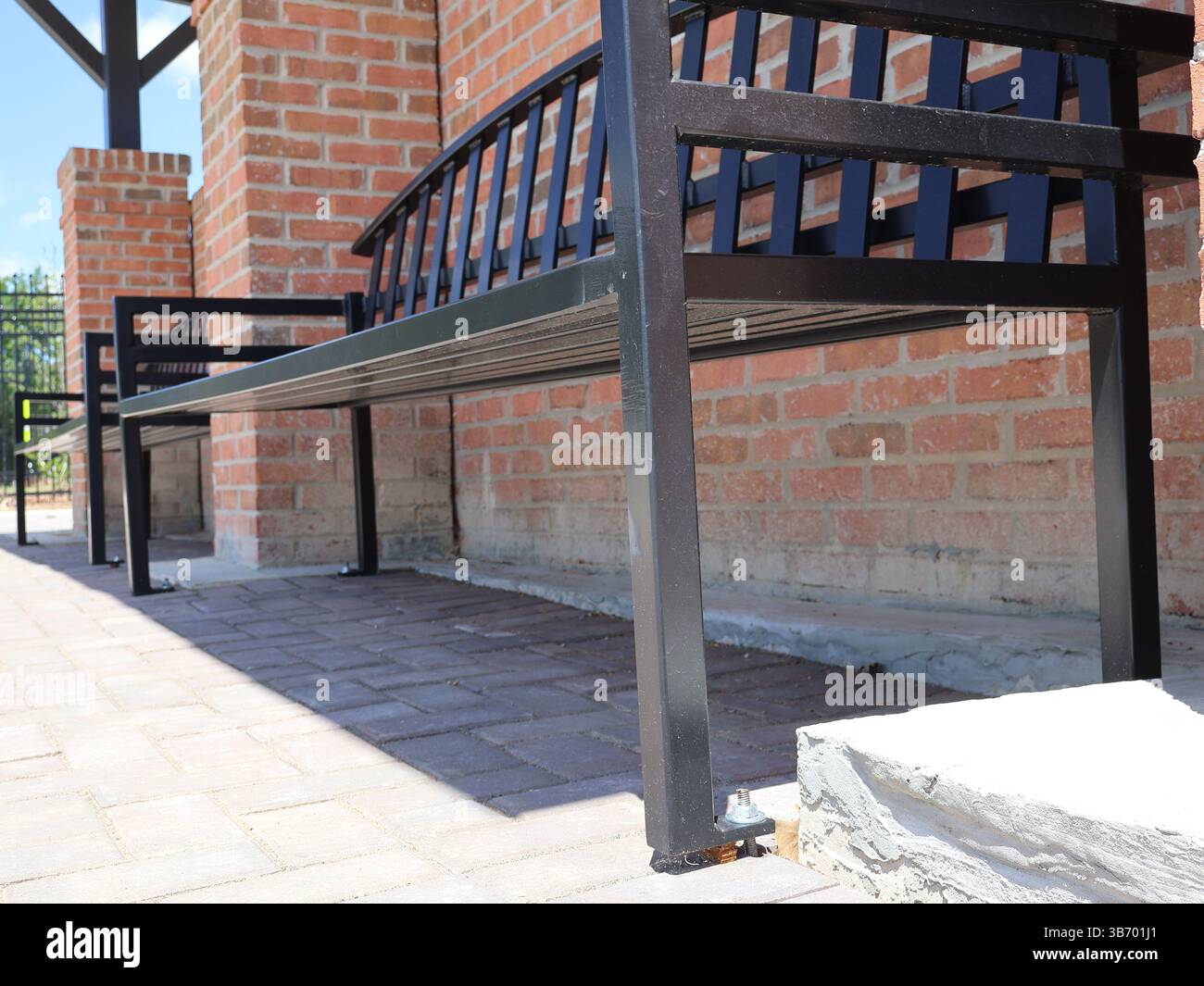 panchine in metallo nero con sedili e schienali a doghe ancorati a lastricatrici in mattoni vicino a mattoni rossi in un tradizionale motivo in muratura con una vista ravvicinata di l Foto Stock