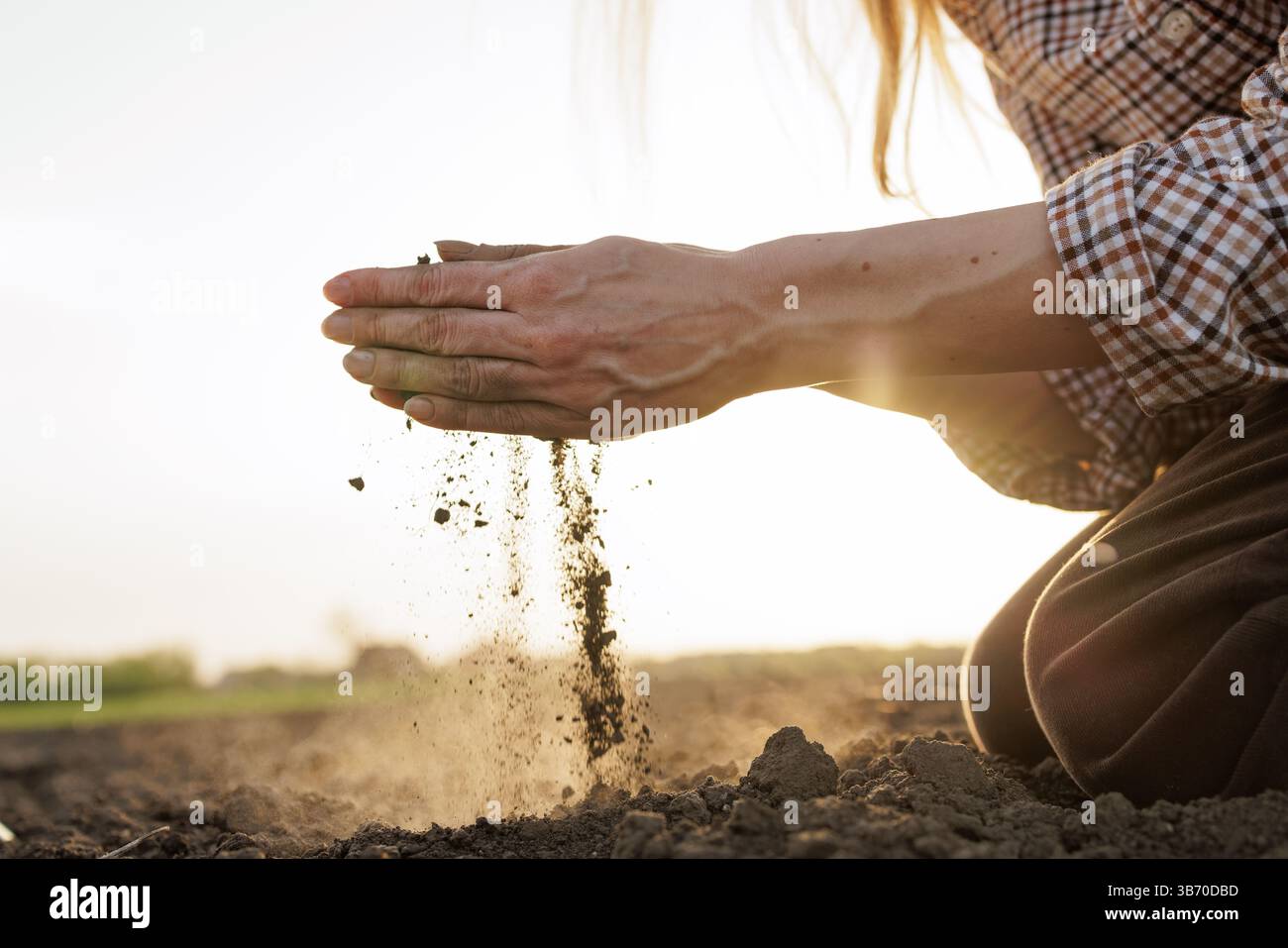 Le mani degli agricoltori analizzano la qualità del suolo al tramonto, simboleggiando l’agricoltura sostenibile e la gestione del territorio. Foto Stock