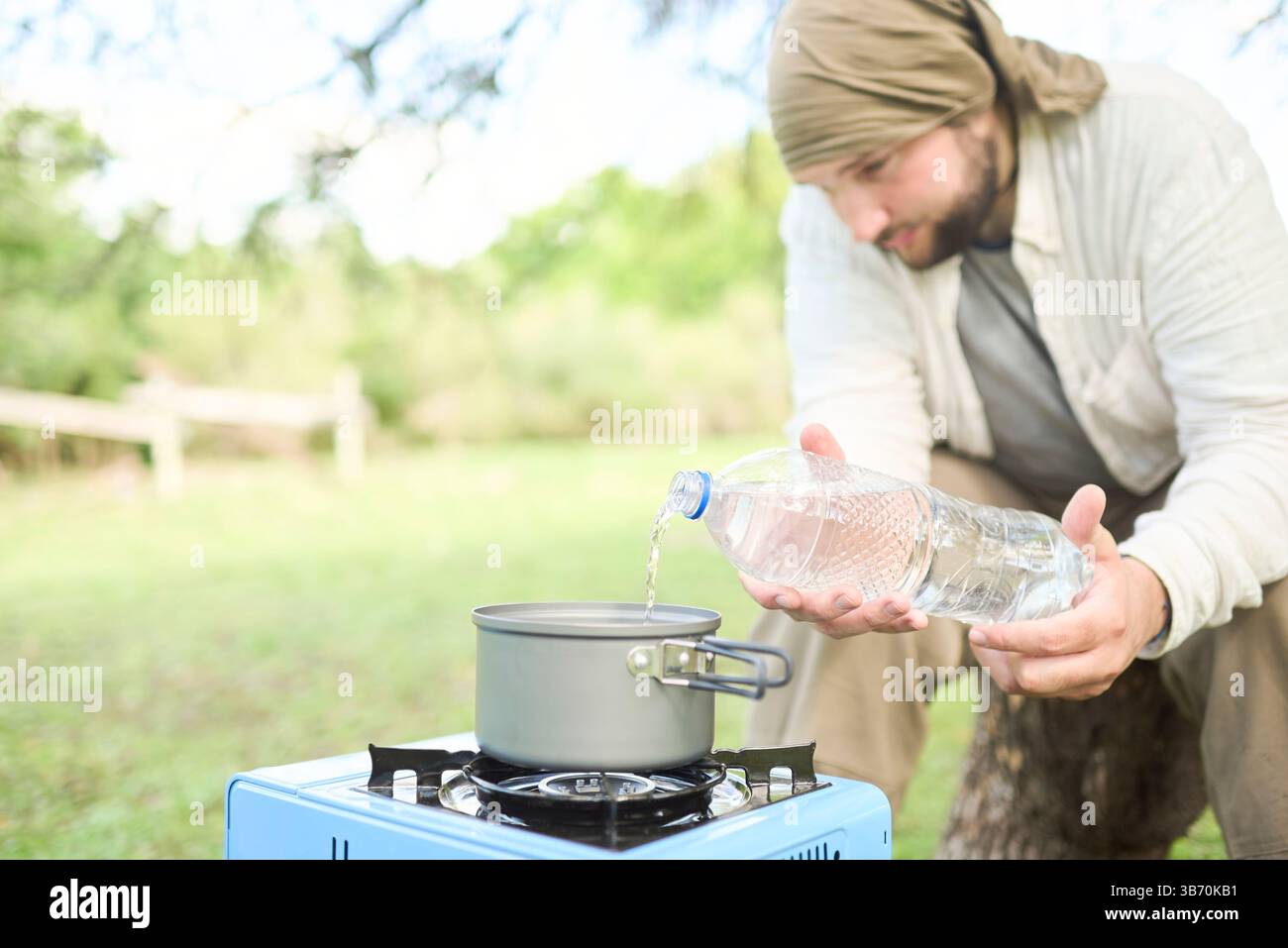 Persona che versa acqua potabile in una pentola come parte del processo di cottura all'aperto, in una stufa a gas portatile, durante il campeggio. Attenzione selettiva all'acqua. Foto Stock