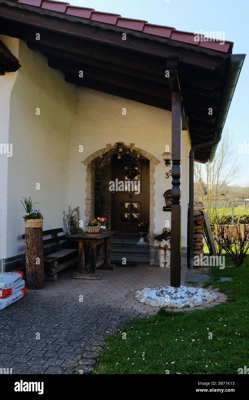 tradizionale casa di campagna europea con tetto piastrellato, portico in legno e giardino curato in un ambiente rurale primaverile. Foto di alta qualità Foto Stock