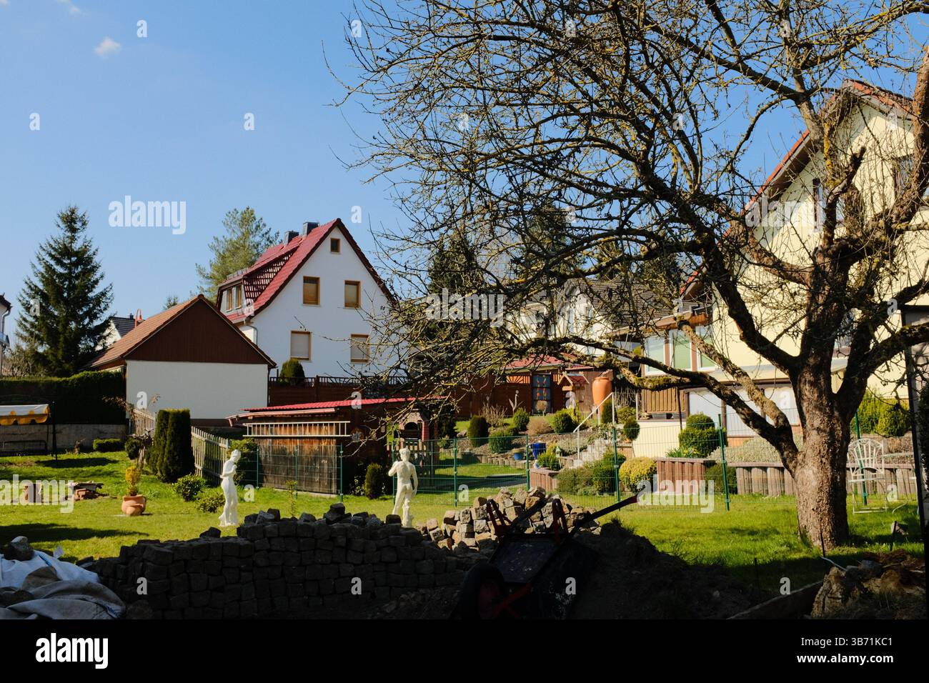 giardino del villaggio europeo decorato con statue bianche del coniglio pasquale e vegetazione primaverile sotto il cielo limpido. Foto di alta qualità Foto Stock