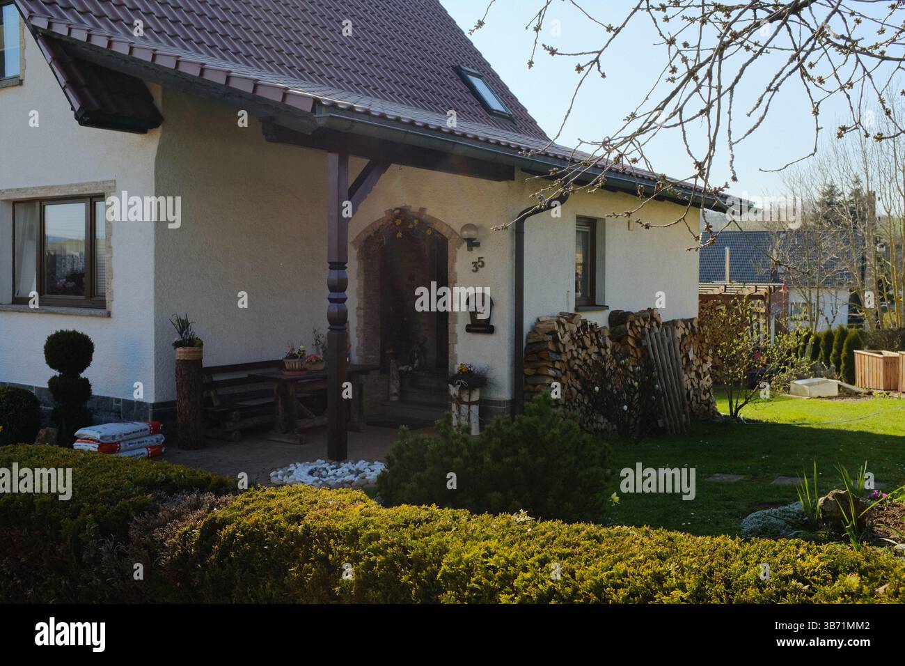 tradizionale casa di campagna europea con tetto piastrellato, portico in legno e giardino curato in un ambiente rurale primaverile. Foto di alta qualità Foto Stock