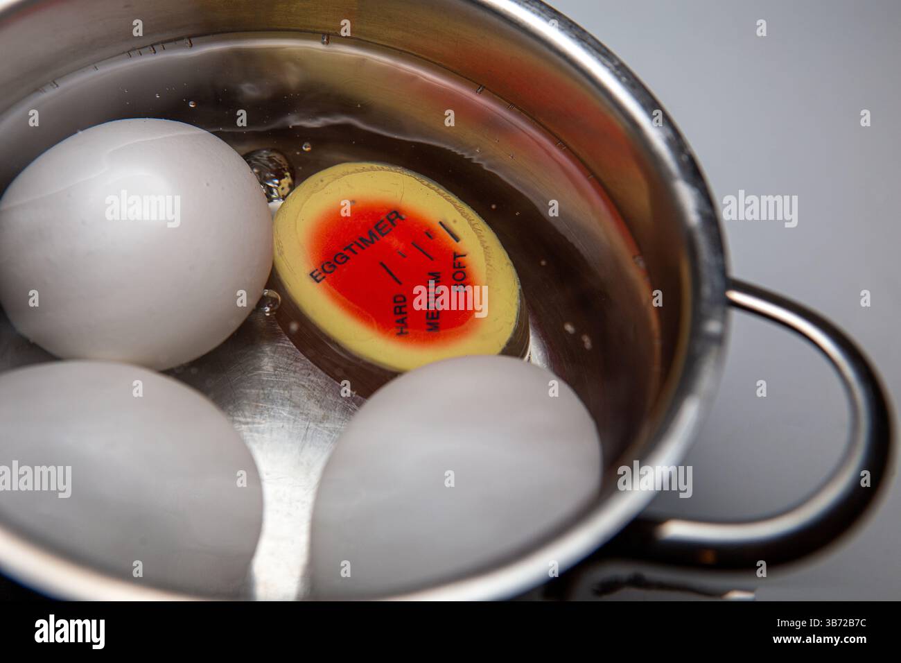 Tre uova fresche bollite in una pentola di acciaio inossidabile, con un timer per uova sommerso che mostra chiaramente l'impostazione "morbida". Foto Stock
