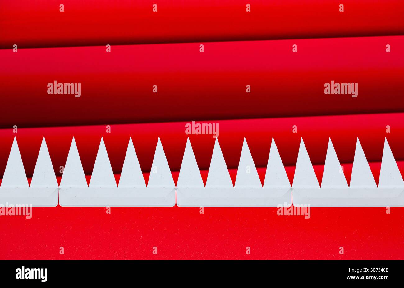 Denti bianchi appuntiti triangolari sporgenti in una fila di rosso, su uno sfondo a strisce rosse. Foto Stock