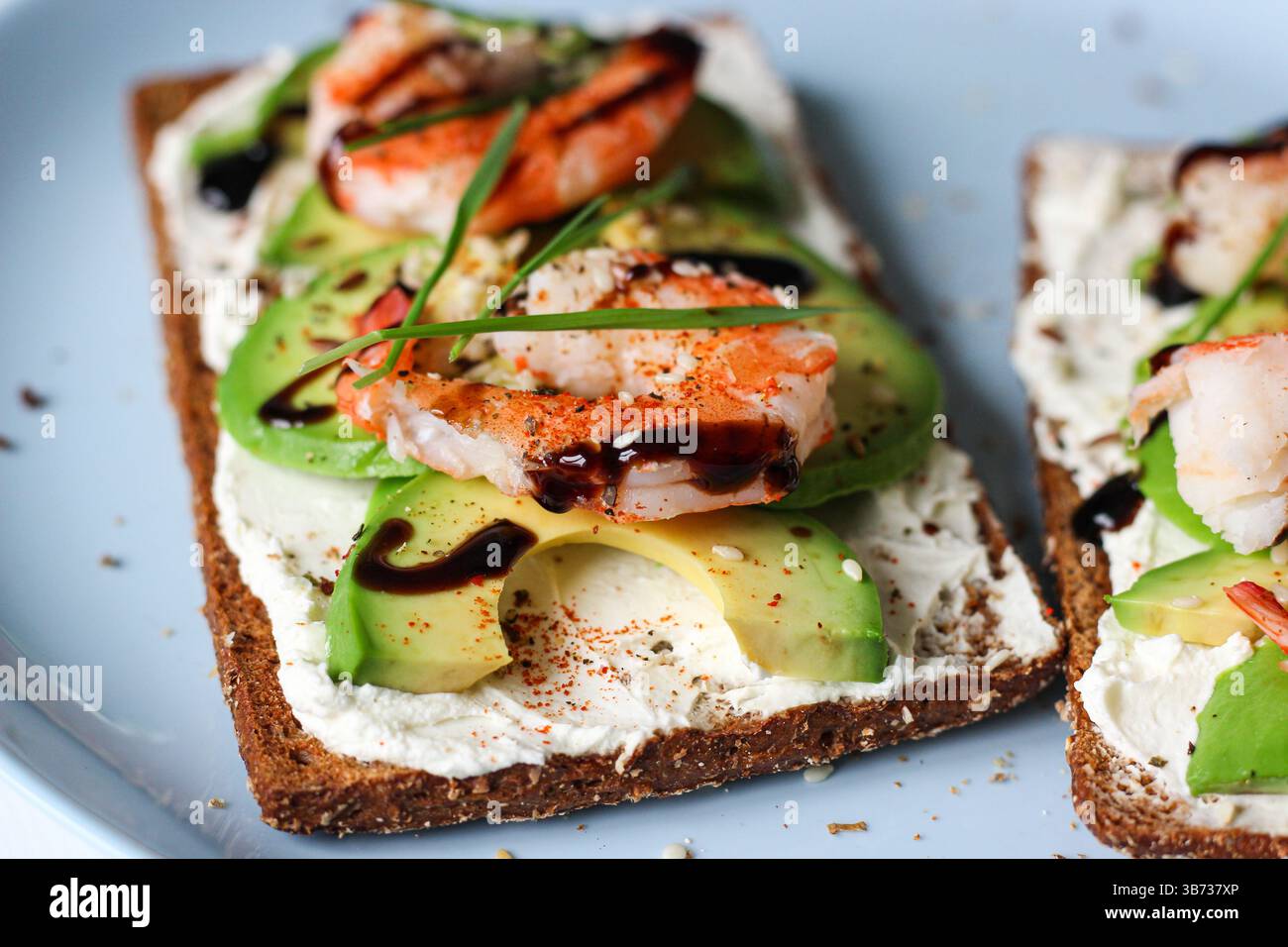 Delizioso panino aperto con formaggio cremoso, avocado, gamberi e glassa balsamica sul pane integrale. Ricoperto di sesamo e microverdure di frumento Foto Stock