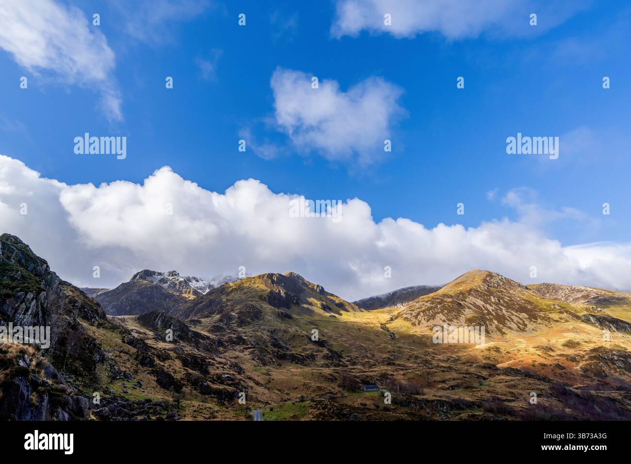 Vista distante delle vette di Cwm Idwal incorniciate da nuvole di cumulus su pendii di ghiaia illuminati dal sole e praterie autunnali Foto Stock