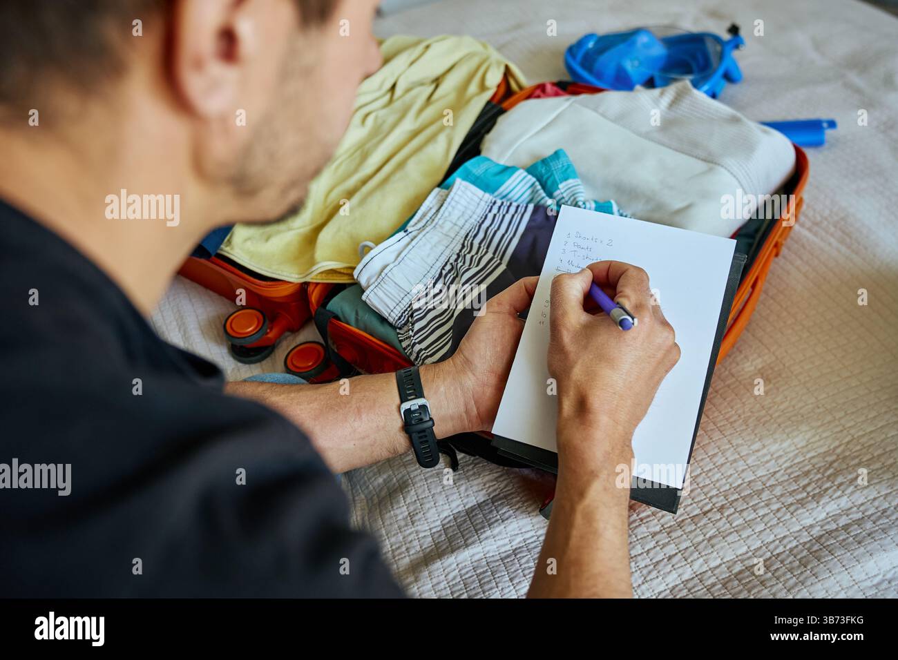 Uomo che si prepara per il viaggio, imballando la valigia con vestiti e controllando la lista d'imballaggio di viaggio. Concetto di pianificazione delle vacanze e delle vacanze Foto Stock