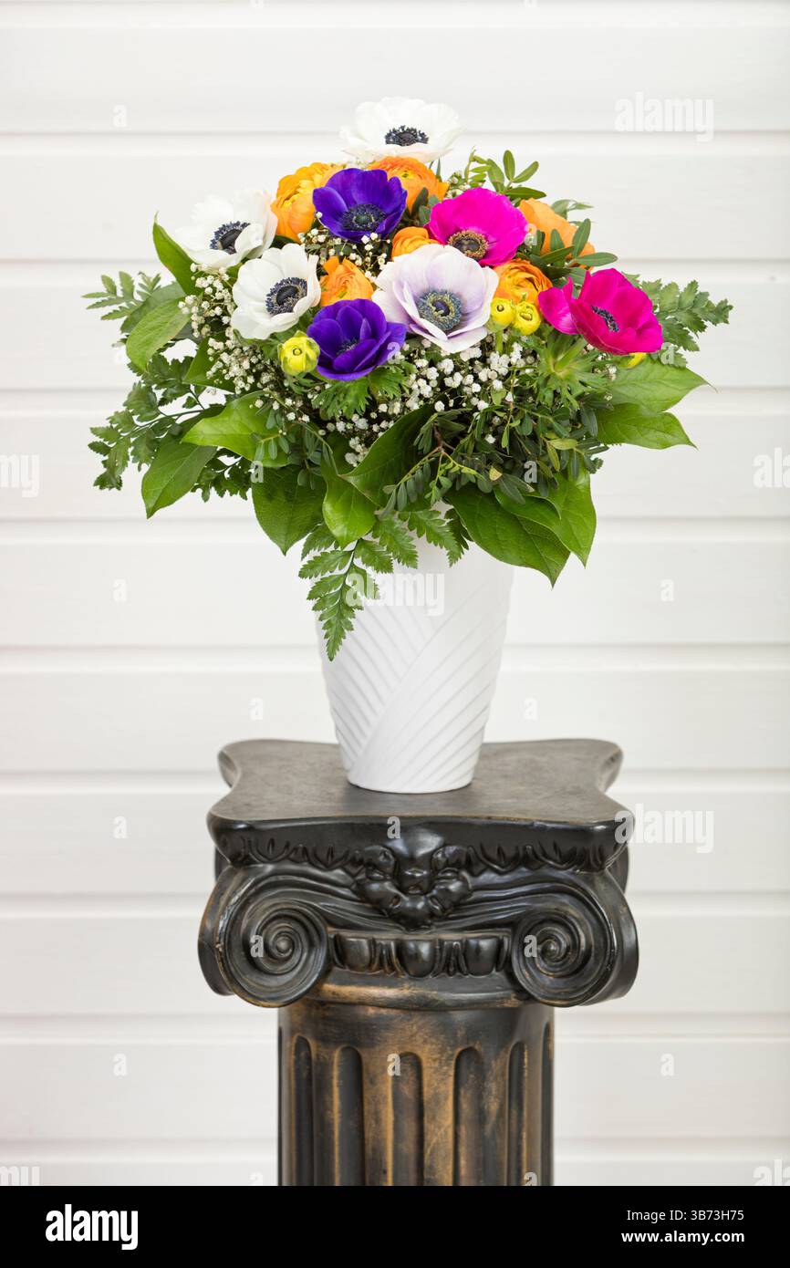 Bouquet colorato con tazze e anemoni di papavero in vaso su piedistallo a colonna antiquato Foto Stock