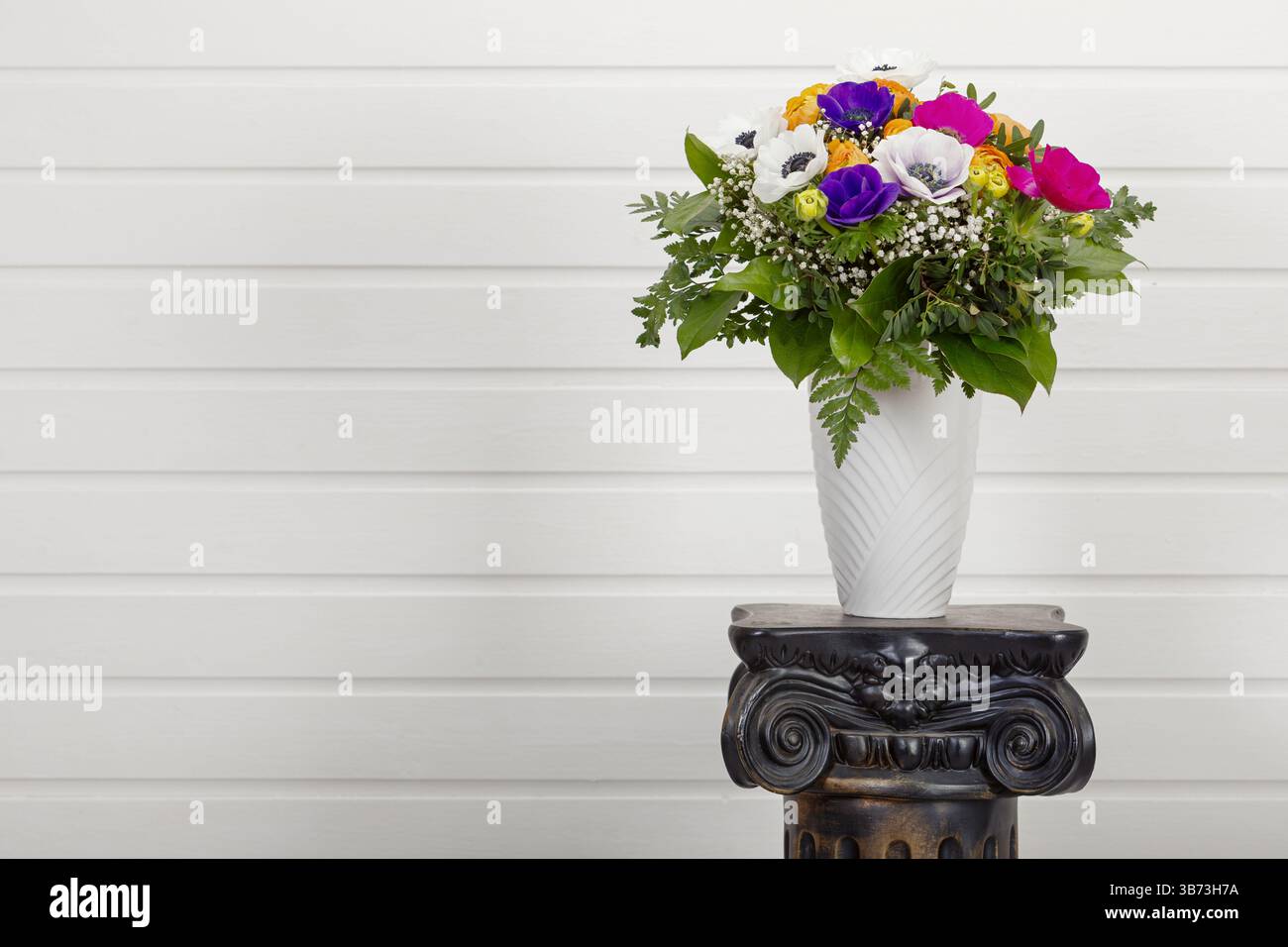Bouquet colorato con tazze e anemoni di papavero in vaso su piedistallo di colonne antiquato con spazio per le copie sulla parete bianca Foto Stock