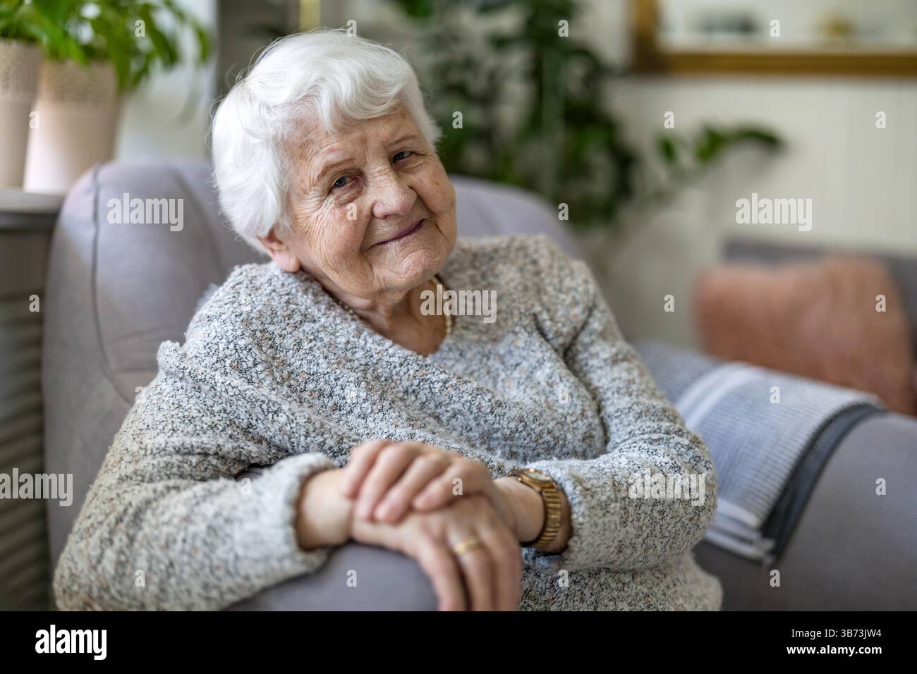 Donna anziana a casa sua seduta in poltrona e guardando la macchina fotografica Foto Stock