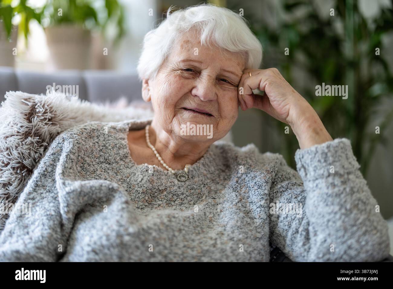 Donna anziana a casa sua seduta in poltrona e guardando la macchina fotografica Foto Stock