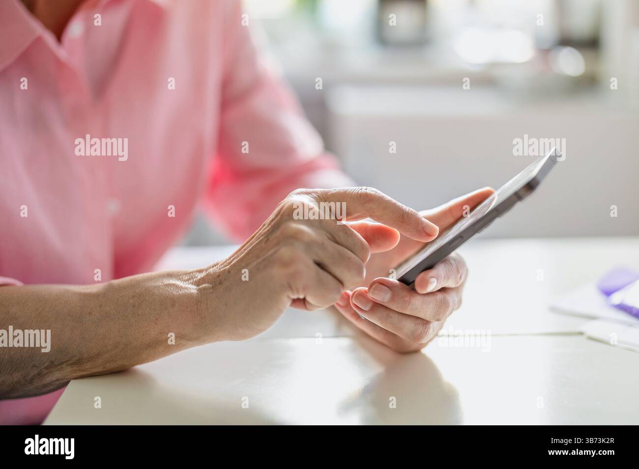 Primo piano delle mani di una donna anziana utilizzando un telefono cellulare al tavolo della cucina Foto Stock