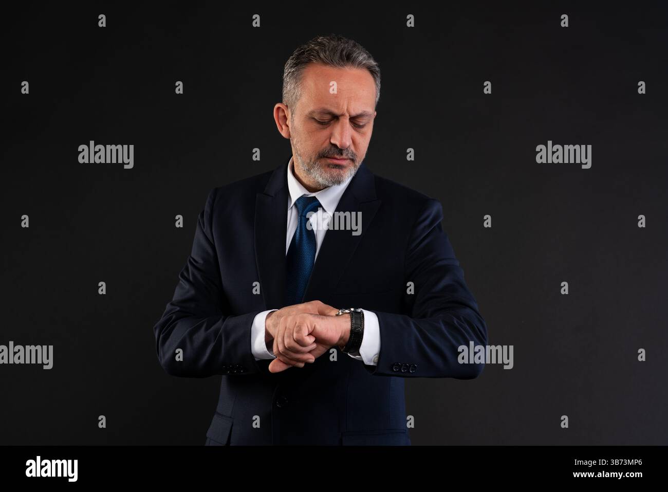 Uomo d'affari maturo in costume che guarda il suo orologio da polso, simboleggia la gestione del tempo, la puntualità o l'urgenza. Foto Stock