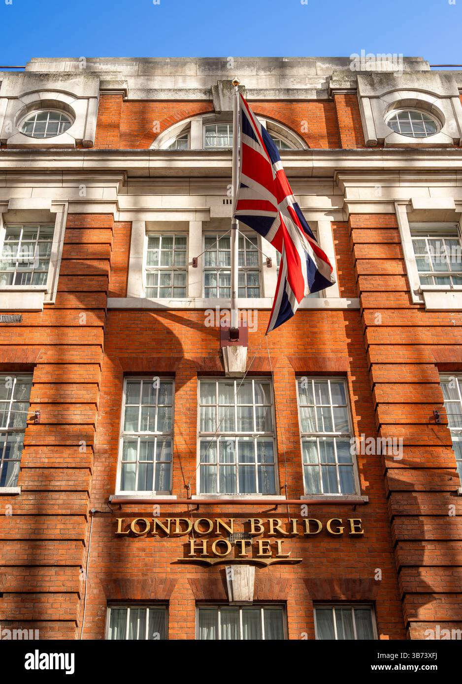 Londra, Regno Unito - 28 aprile 2025: Facciata del London Bridge Hotel con bandiera Union Jack, esterno in mattoni rossi e cielo blu. Foto Stock