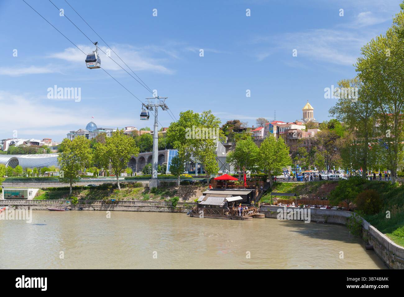 Tbilisi, Georgia - 29 aprile 2019: Una pittoresca vista di una città che presenta funivie, un tranquillo lungofiume e una vibrante vegetazione sotto un blu chiaro Foto Stock Tbilisi, Georgia - 29 aprile 2019: Una pittoresca vista di una città che presenta funivie, un tranquillo lungofiume e una vibrante vegetazione sotto un blu chiaro Foto Stock